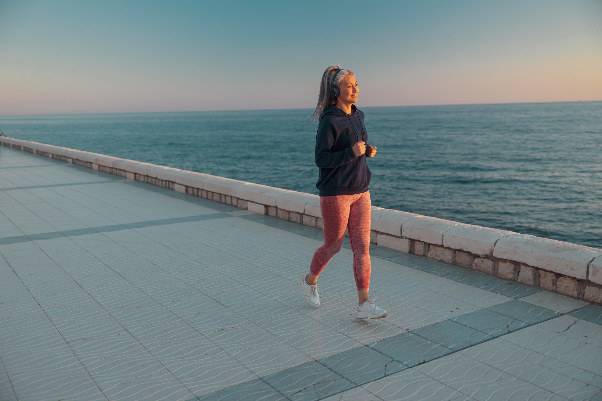 Asian sportswoman in black hoodie jogging on the embankment