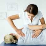 attractive chiropractor touching hand of patient in grey t-shirt