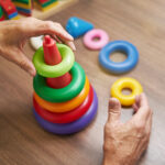 Cropped view on hands of mature man collecting colored toy pyramid for recovery adaptive skills at neurological rehabilitation facility