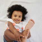 Overhead Shot Of Smiling Baby Girl Lying On Bed