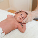 Physiotherapist performing coronal suture work on a newborn baby in a therapy center. Health care and medical concept.