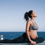 Pregnant woman doing yoga exercise routine next to the beach - Concept of maternity and healthy lifestyle